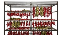 Wooden drying rack filled with red chili peppers and green herbs hanging to dry, traditional food preservation method for culinary and agricultural use.