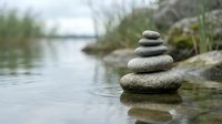 Zen stone stack balanced on water edge with natural lake background for meditation and wellness concepts.