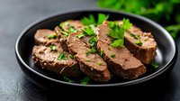 Tender sliced beef tenderloin medallions garnished with fresh parsley served on black plate against dark background, gourmet restaurant presentation.