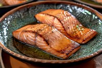 Grilled salmon fillets with sesame seeds and glaze served on traditional ceramic plate. Close up view of juicy fish with crispy skin and caramelized surface.