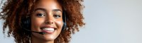 Young African American woman with natural curly hair wearing headset and smiling. Customer service representative with positive friendly expression on gray background.