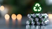 Stack of AA batteries with glowing green recycling symbol above on dark background with bokeh lights, promoting environmental sustainability and proper disposal.