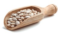 Dried pinto beans in wooden scoop on white background, raw legumes for cooking healthy protein-rich meals.