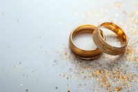 Golden wedding rings with textured and smooth surfaces on light background with scattered glitter, romantic symbol of marriage and eternal love.