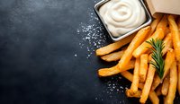 Crispy golden french fries with rosemary sprig and creamy mayonnaise dipping sauce on dark stone background with salt crystals and copy space.
