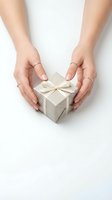Female hands protecting small gift box with ribbon bow on white background for holidays and special occasions.