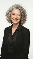 Confident mature businesswoman with curly gray hair smiling in black blazer against neutral background for professional corporate headshot.