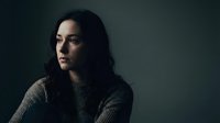 Young Hispanic woman with dark wavy hair wearing gray knit sweater in moody dramatic lighting against dark background for emotional storytelling concepts.