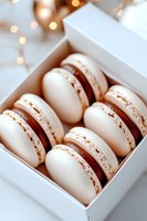 White chocolate macarons with brown filling arranged in gift box against blurred festive lights background, elegant dessert presentation for special occasions.