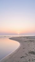 Serene beach sunset with pastel sky reflecting on wet sand and gentle waves creating peaceful coastal atmosphere for relaxation and meditation concepts.