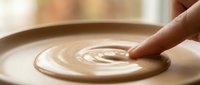 Finger touching creamy coffee latte art with swirled foam design in cup, close-up of barista creating decorative pattern on hot beverage.