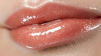 Close up view of glossy coral pink lips with wet shine effect and smooth texture showing professional makeup application and beauty cosmetics result.