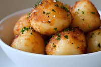 Golden roasted baby potatoes garnished with fresh herbs in white ceramic bowl, close-up view showing crispy exterior and tender interior.
