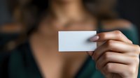 Female hand holding blank white business card against dark background, showcasing elegant manicure and formal attire for professional networking.