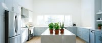 Modern kitchen with light blue cabinetry, white countertops, stainless steel appliances, and potted plants on island for home design and interior decoration projects.