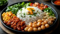 Brazilian rice bowl with beans, sunny side up egg, corn, chickpeas and fresh herbs served on dark plate. Healthy protein-rich vegetarian meal.