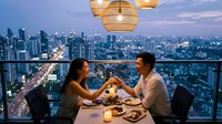 Romantic couple enjoying intimate dinner on luxury rooftop terrace with city skyline view at twilight, fine dining restaurant atmosphere with elegant lighting.