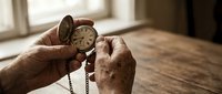 Elderly hands holding vintage pocket watch on wooden table in warm natural light. Concept of time, memories, aging, nostalgia and life reflection.