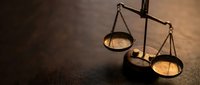 Vintage brass scales of justice on dark wooden surface with warm lighting creating dramatic shadows for legal and law firm concepts.