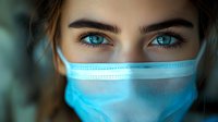 Close up portrait of young woman wearing protective medical face mask with bright blue eyes looking at camera. Healthcare concept during pandemic.