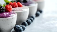 Fresh berry smoothie bowls with yogurt, topped with raspberries, blackberries and blueberries on light marble background, healthy breakfast concept.