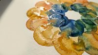 Watercolor paint palette with vibrant orange, blue and green pigments mixed on white paper surface for artistic projects and creative painting techniques.