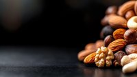 Mixed raw nuts scattered on dark background with copy space, selective focus on almonds, walnuts, hazelnuts and cashews creating gourmet food composition.