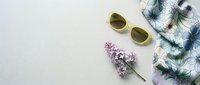 Flat lay of yellow sunglasses, lilac flowers, and floral scarf on light gray background, spring fashion accessories arrangement with copy space.