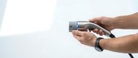 Male hands holding modern electric vehicle charging plug connector against white background for sustainable transportation and eco-friendly automotive technology.
