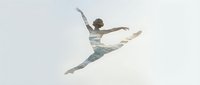 Young male dancer performing grand jete leap against white background. Athletic ballet performer in casual attire showcasing graceful movement and flexibility.