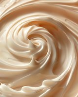 Creamy swirled texture of white chocolate or vanilla mousse in spiral pattern, macro close up view showing smooth glossy surface and soft flowing curves.