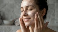 Young woman applying exfoliating face scrub mask in bathroom, skincare routine, spa treatment, natural beauty care, wellness self-care ritual.