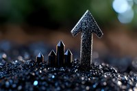 Black glittery arrow pointing upward with small crystal formations rising from sparkly ground, symbolizing growth and success against dark bokeh background.