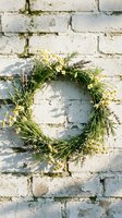 Rustic evergreen wreath with small white flowers hanging on weathered white brick wall for seasonal home decor and holiday celebrations.