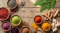 Colorful superfood ingredients in wooden bowls on rustic table including turmeric, goji berries, chia seeds, spirulina and fresh ginger root for healthy cooking.