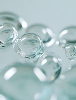 Transparent water drops or bubbles on light turquoise background with soft focus and bokeh effect, macro photography showing surface tension and reflection.