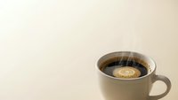 Steaming hot coffee cup with rich dark brew on neutral beige background for morning beverage and cafe marketing materials.