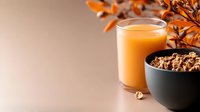 Orange juice in glass with granola cereal bowl and autumn dried flowers on beige background, suitable for breakfast, nutrition, and wellness marketing materials.