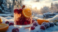Festive winter cocktail with cranberries, orange slice and cinnamon in glass on snowy background with golden sunset light. Fresh garnish and frost covered berries.