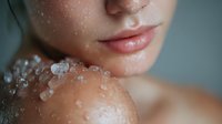 Close-up of woman's face and shoulder with water droplets or salt crystals on skin, showcasing hydrated lips and dewy complexion in soft, natural lighting.