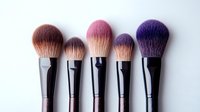 Professional makeup brushes with soft synthetic bristles in pink and purple ombre colors arranged in row on white background, cosmetic tools for beauty application.