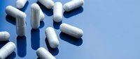 White and blue capsule pills scattered on light blue background with shadows for medical and pharmaceutical design concepts.