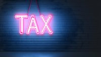 Pink neon tax sign glowing against dark blue brick wall background, creating modern urban nighttime atmosphere for financial and business concepts.