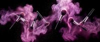 Professional makeup brushes with vibrant pink powder explosion on black background for beauty and cosmetics advertising campaigns.