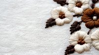 Delicate floral embroidery on natural linen fabric with cream and brown flowers, decorative needlework detail in corner arrangement.