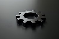 Single metallic gear wheel on dark reflective surface with dramatic lighting and shadow creating industrial minimalist composition for business concepts.