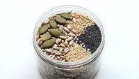 Assorted seeds and grains in glass jar including pumpkin seeds, sesame, poppy and sunflower seeds for healthy cooking and nutrition concepts.