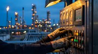 Industrial worker operating control panel at oil refinery during twilight with illuminated petrochemical plant in background for energy sector operations.