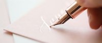 Calligrapher hand holding fountain pen writing elegant stroke on white paper, artistic lettering and penmanship practice.