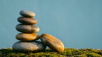 Balanced stack of smooth river stones on moss with soft blue background for meditation wellness and zen lifestyle concepts.